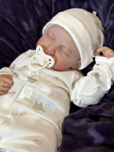 A baby doll lying on a cozy blanket, with a pacifier placed nearby.